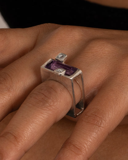 A silver square ring with an amethyst baguette and two square topaz, shown on a hand.