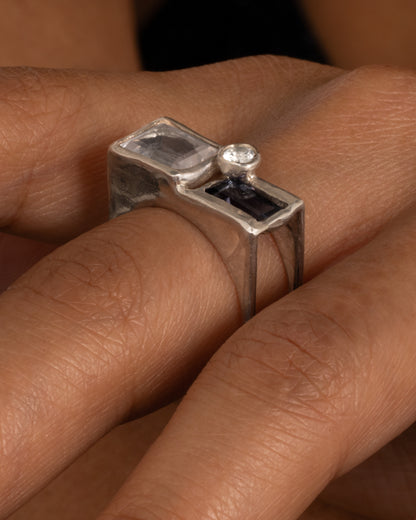 A silver square cage ring with a quartz, iolite, and topaz, shown on a hand.