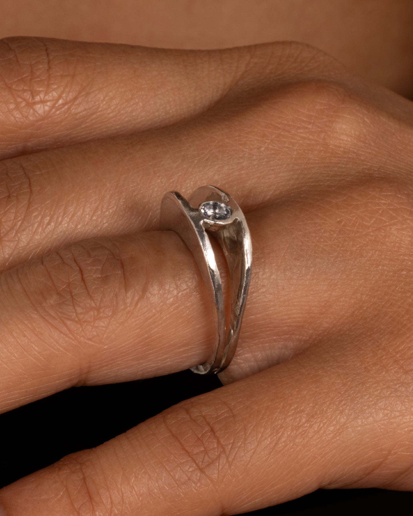 A silver ring with a split shank and a center iolite, shown on a hand.
