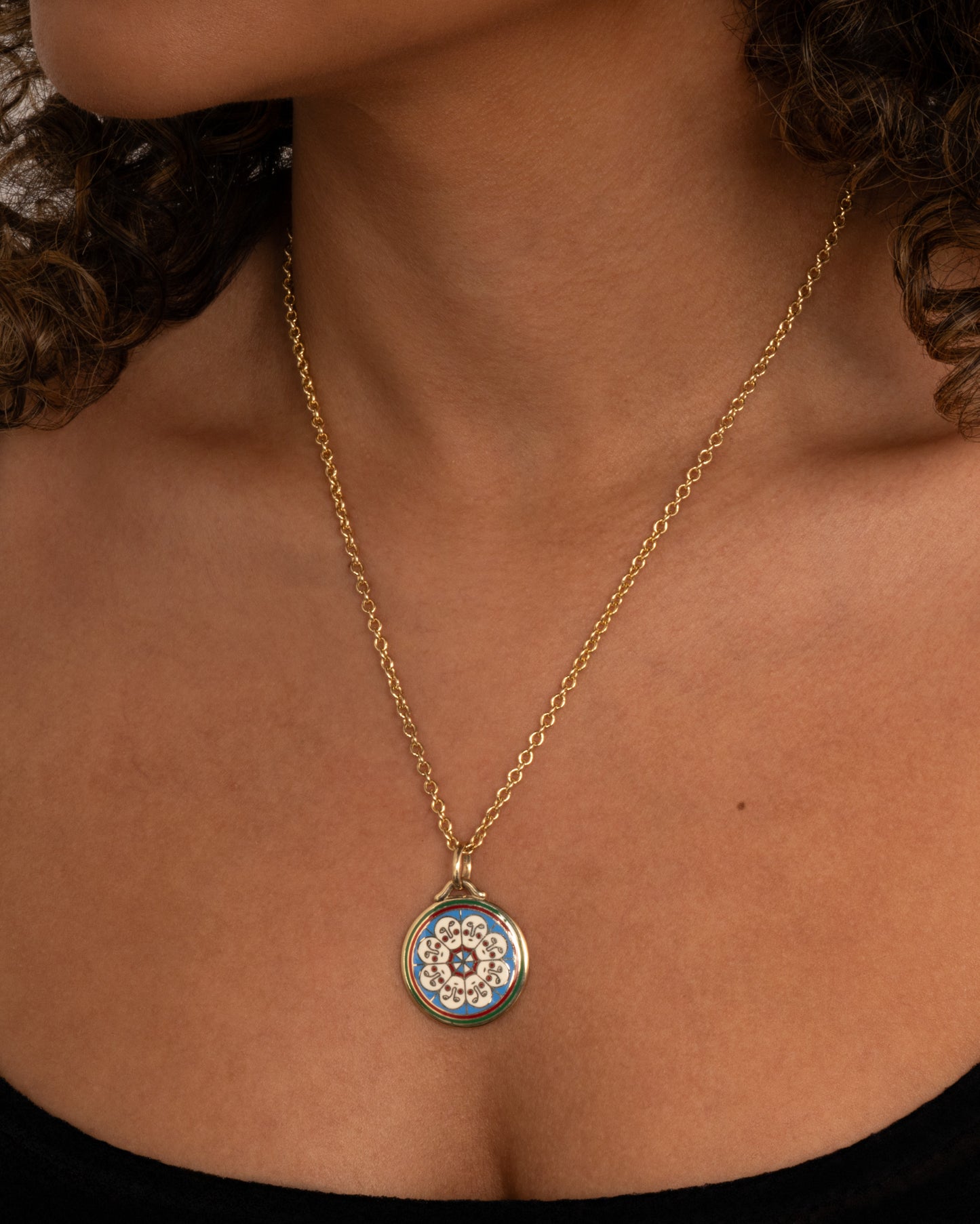 A yellow gold necklace with a circular pendant hanging from it, on it is a circle of white faces in enamel. Shown worn around the neck.
