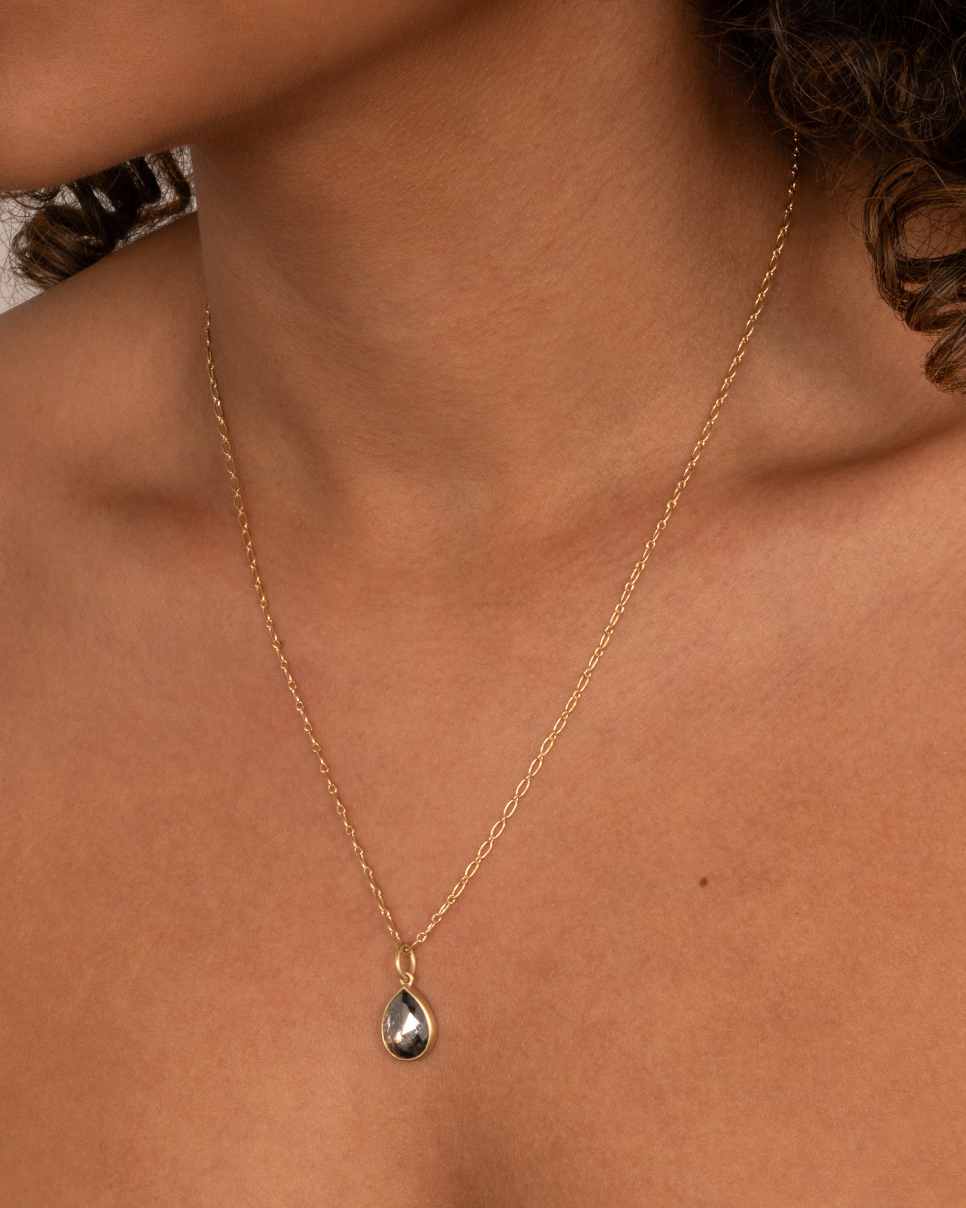 A yellow gold elongated link cable chain necklace with a teardrop shaped salt and pepper diamond, shown on a person.