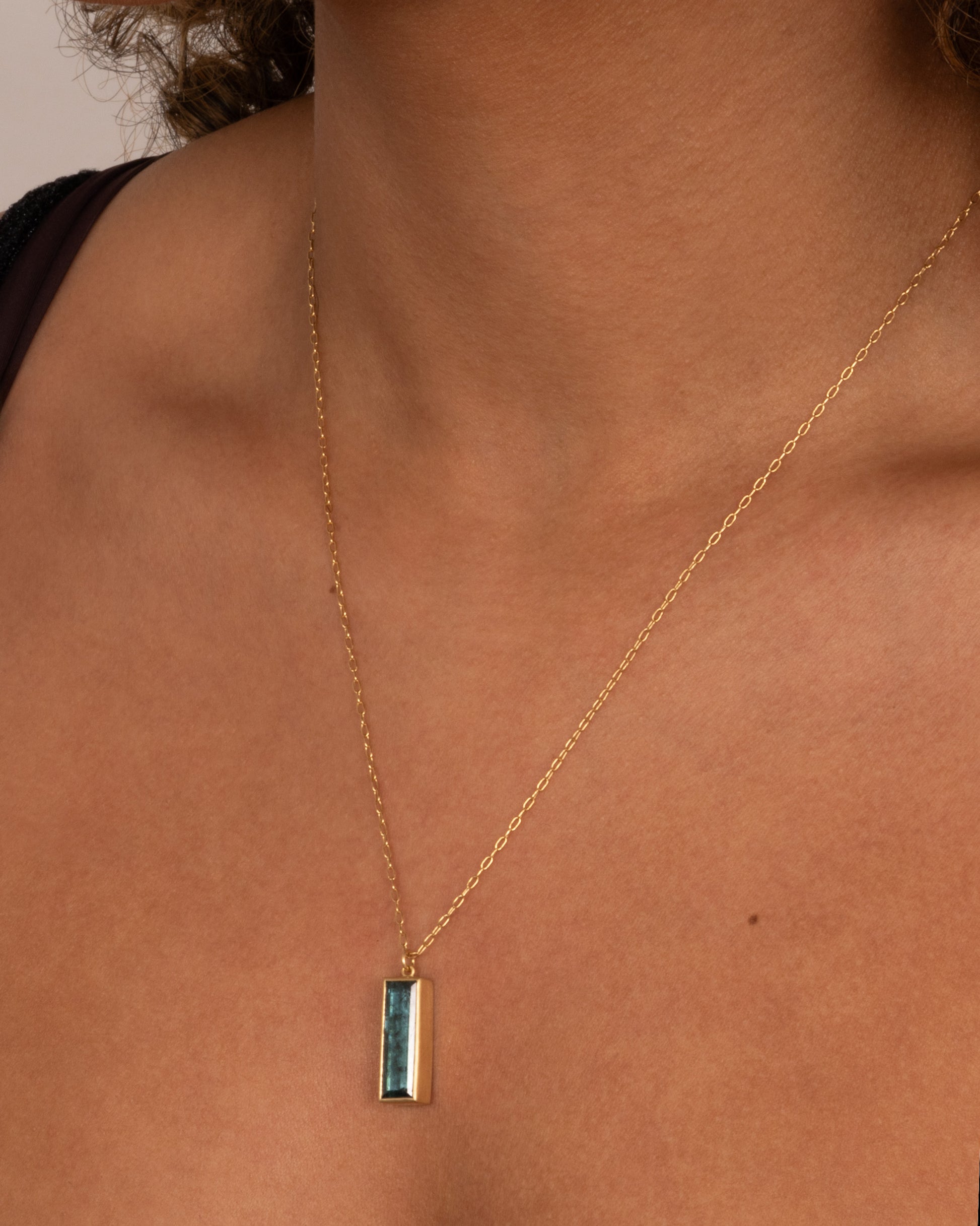 A yellow gold pendant necklace with a blue tourmaline slab, shown on a person.