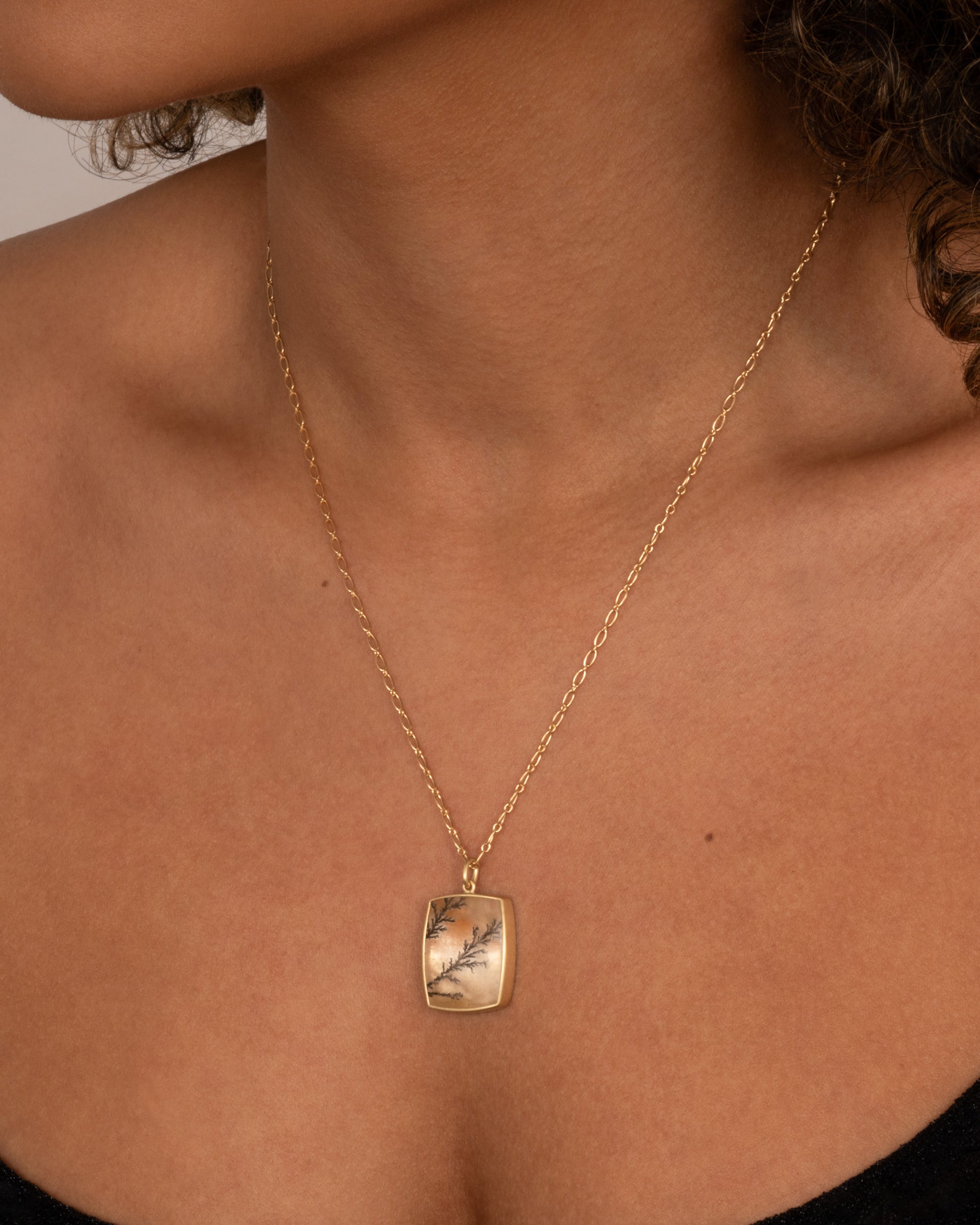 A yellow gold dendritic quartz pendant hanging from an alternating oval chain. Shown worn around a neck.