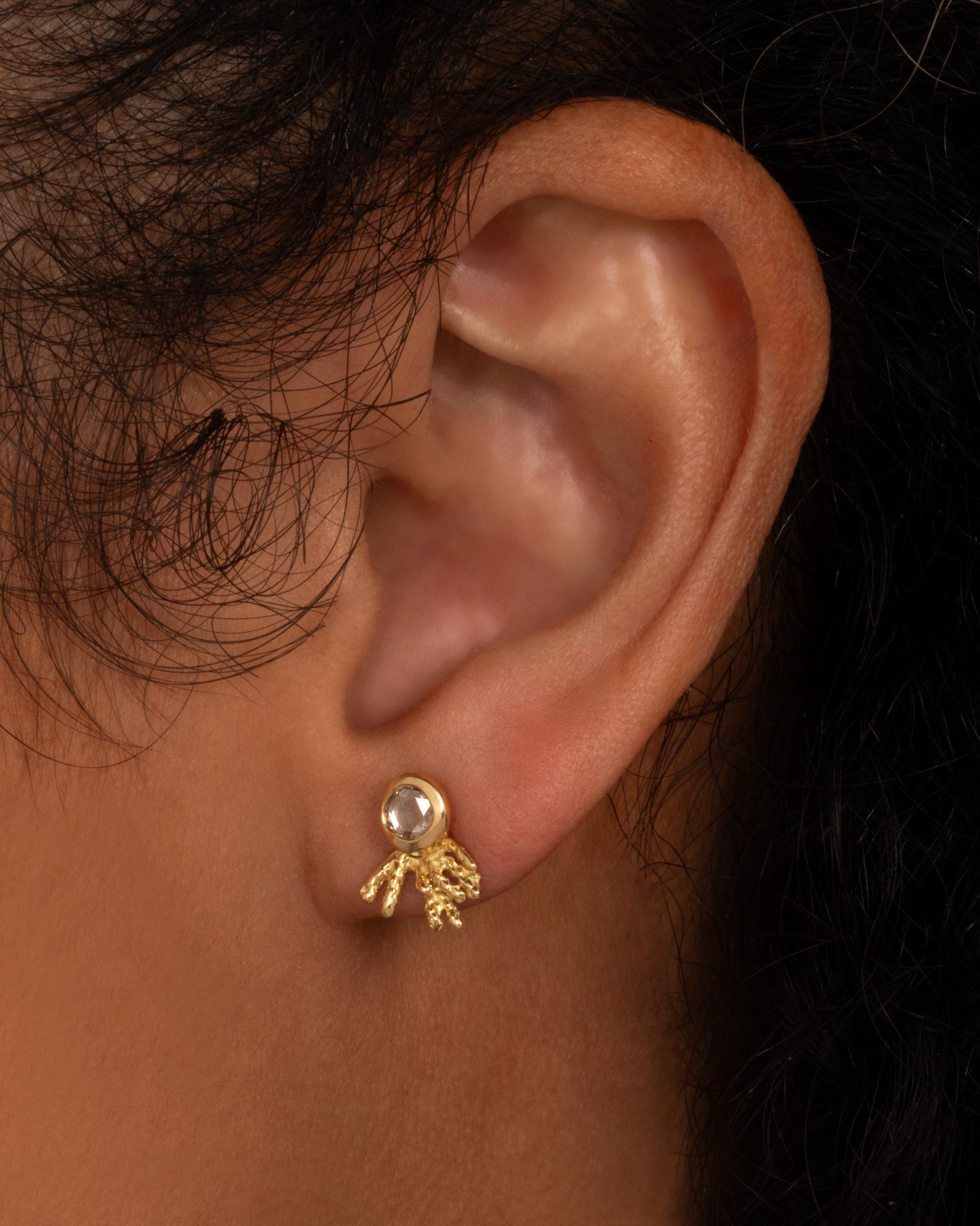 A yellow gold stud earring with a rose cut diamond and yellow gold comet-like tail. Shown on a person.