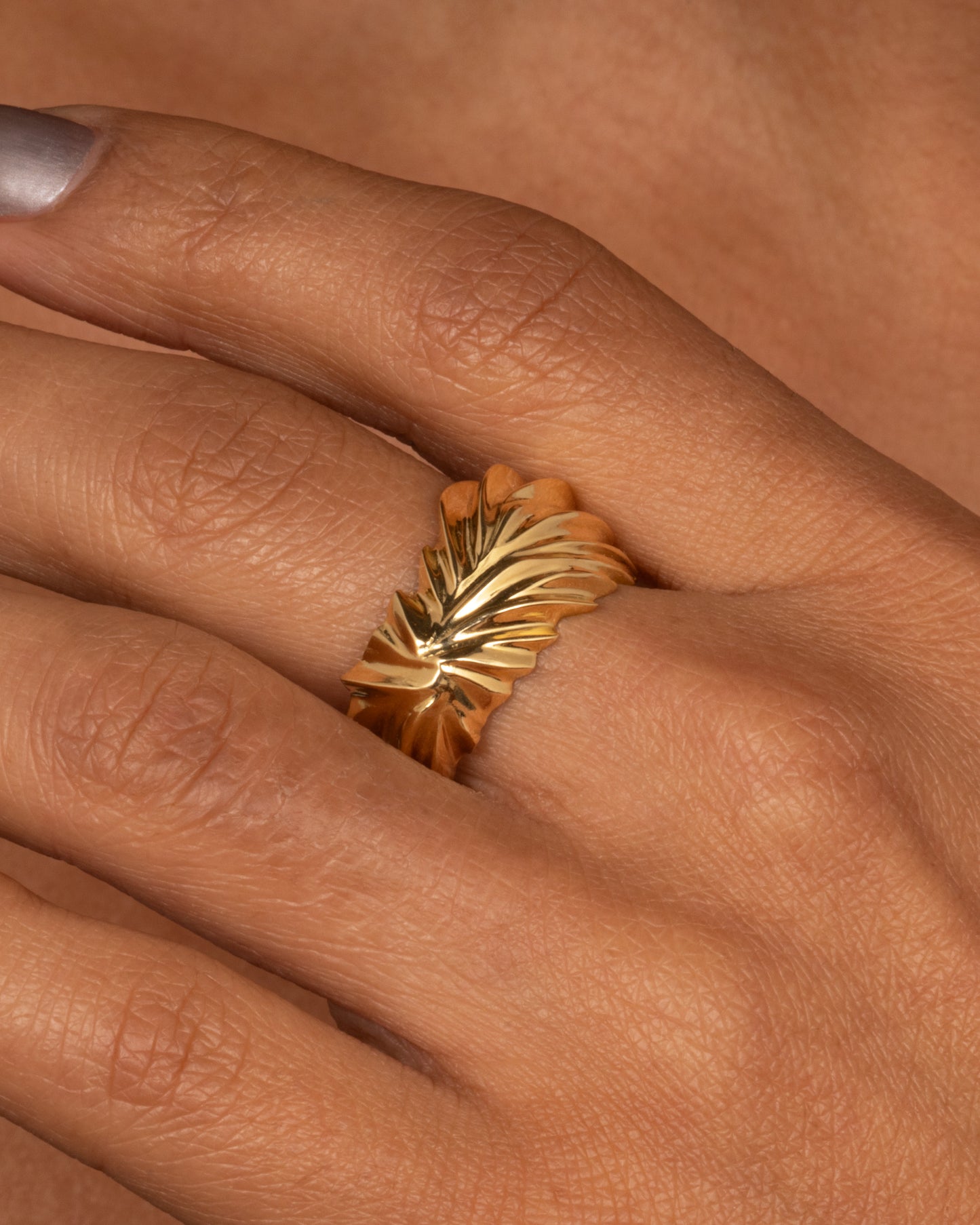 A yellow gold ring with wavy and chevron textures, shown from the front on a hand.