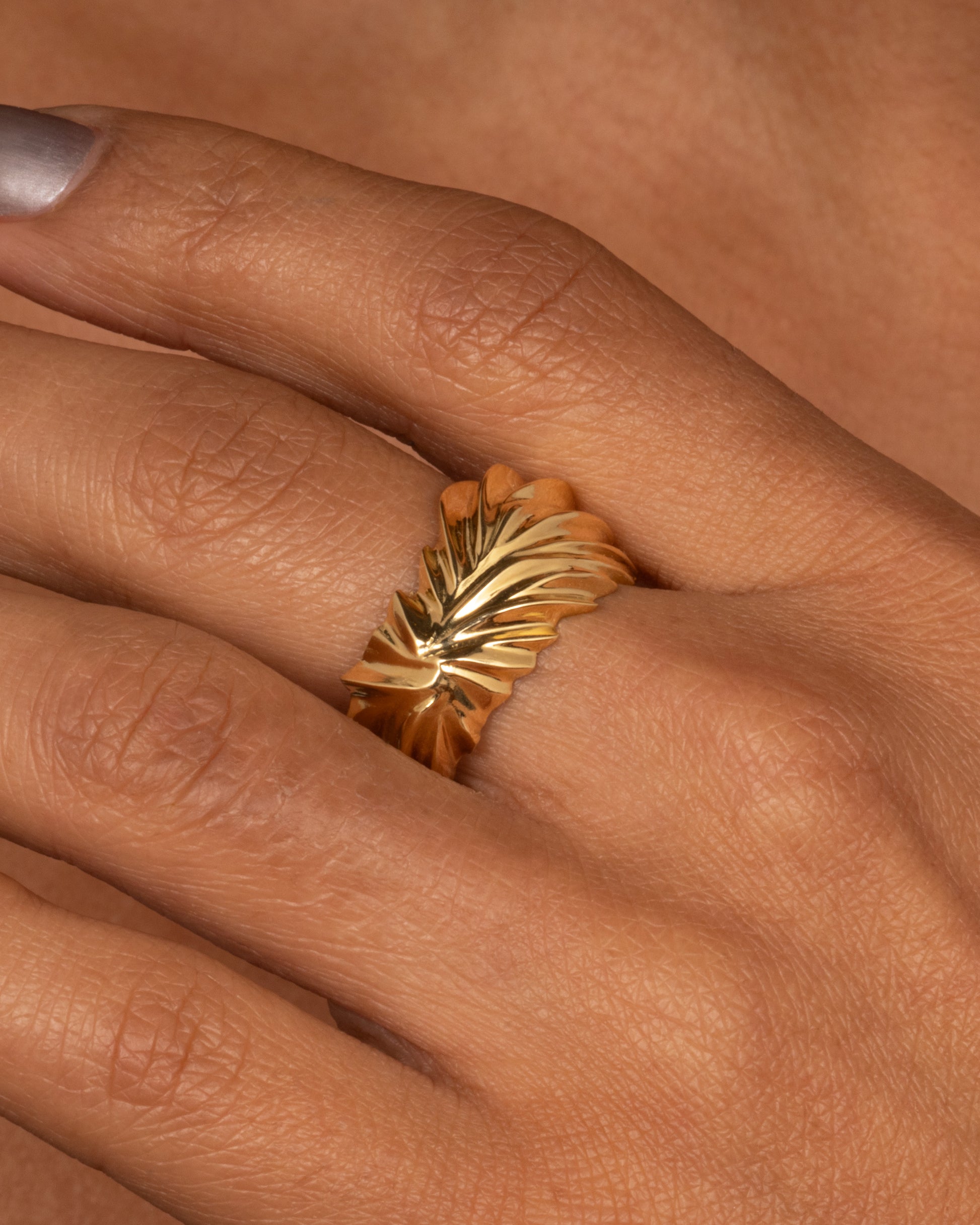 A yellow gold ring with wavy and chevron textures, shown from the front on a hand.