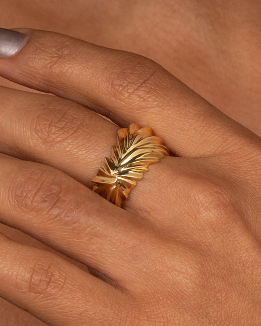 A yellow gold ring with wavy and chevron textures, shown from the front on a hand.