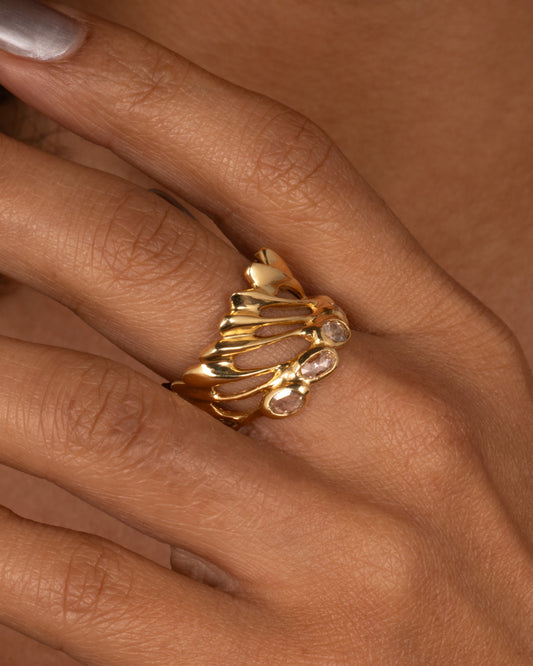 A yellow gold ring with intertwined strands and a queue of rose cut diamonds on its edge, shown on a hand.