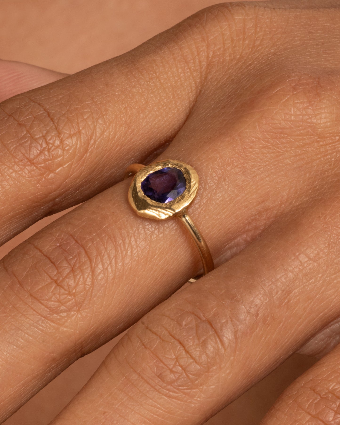 A yellow gold ring with a purple blue sapphire, shown worn on a finger.
