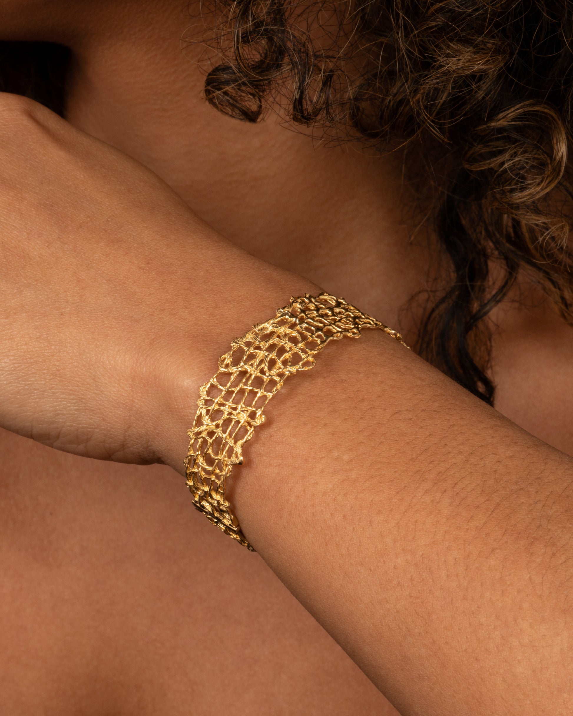 A woven yellow gold wire strand bracelet shown on a person.