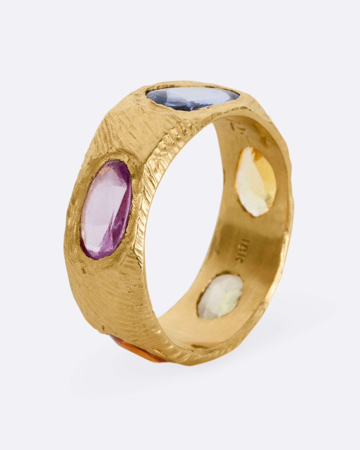 A yellow gold band with rose cut multicolor sapphires all the way around. Shown from the side, standing up.