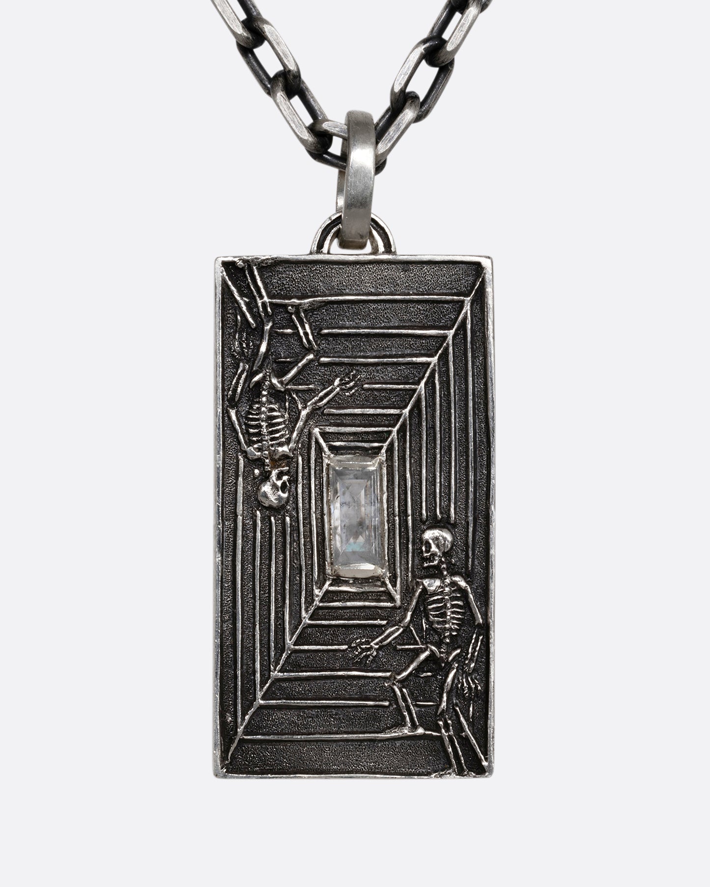 A sterling silver necklace with a rectangular pendant depicting two skeletons and a diamond at the center. Shown from the front.