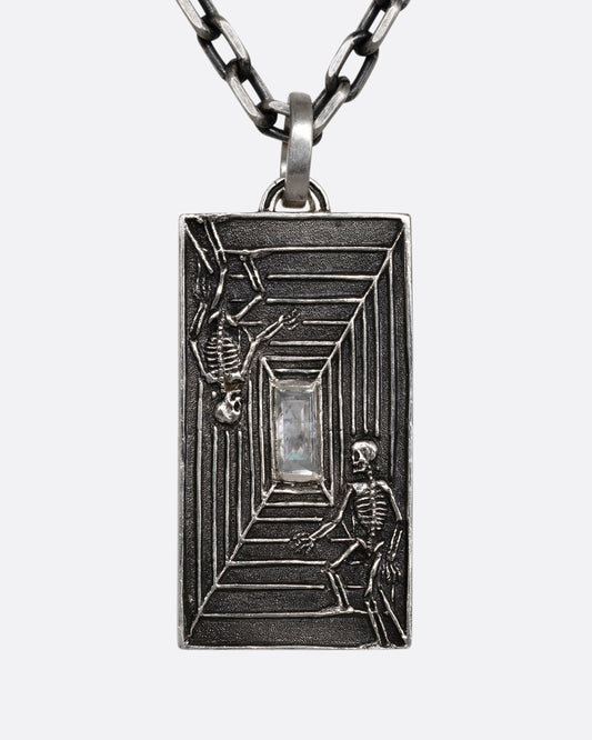 A sterling silver necklace with a rectangular pendant depicting two skeletons and a diamond at the center. Shown from the front.