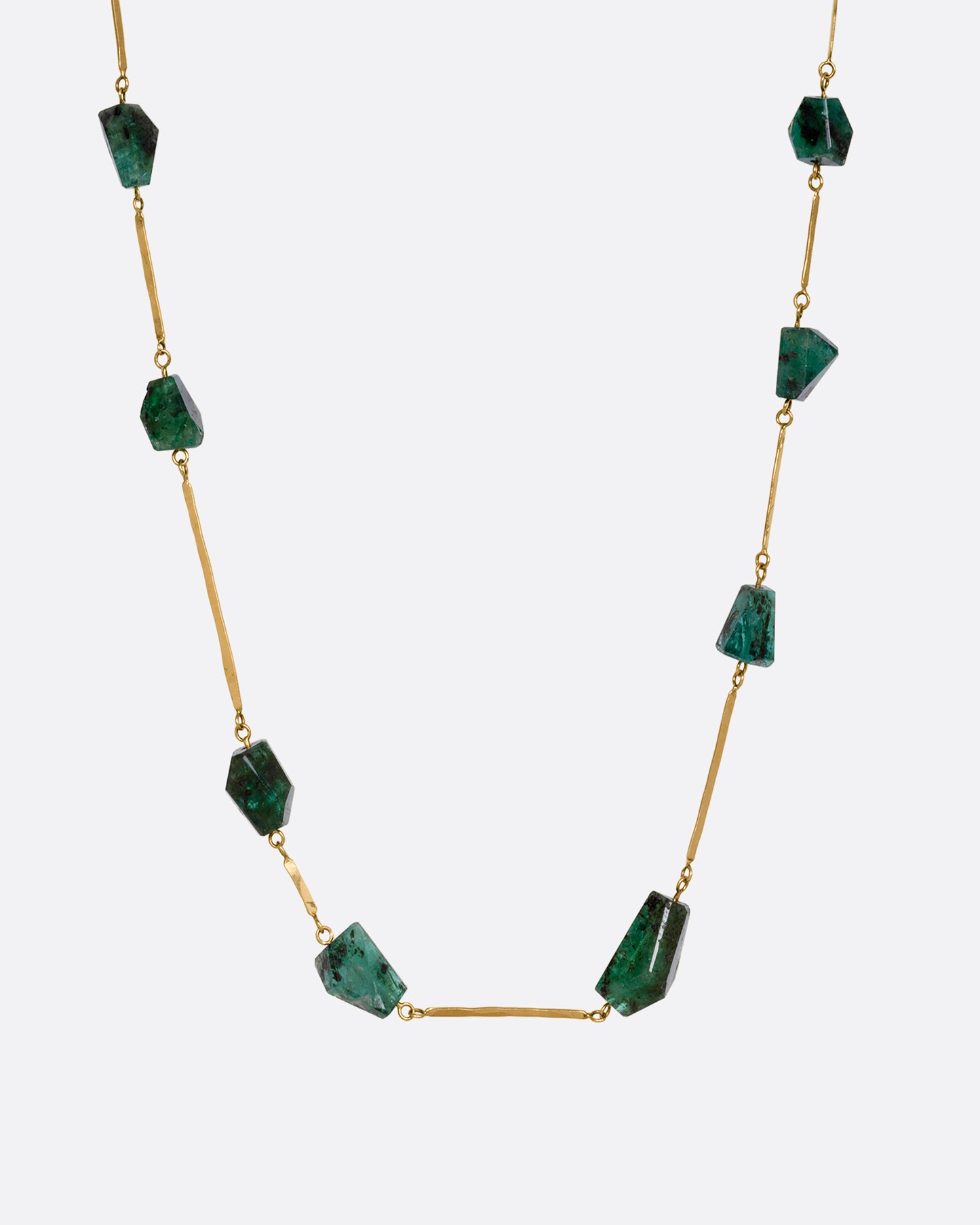 A yellow gold hammered bar link necklace with raw emeralds throughout. Shown from the front.