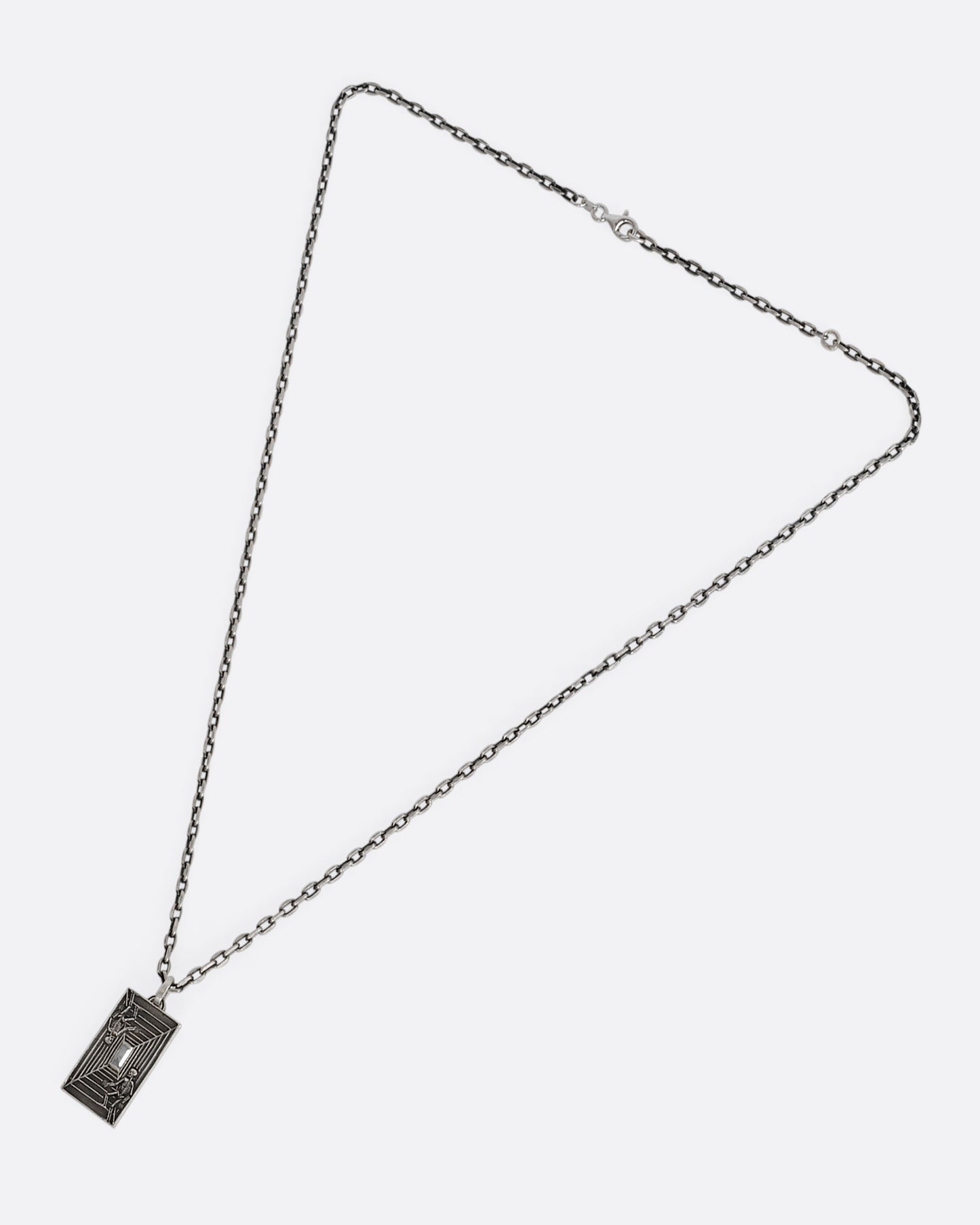 A sterling silver necklace with a rectangular pendant depicting two skeletons and a diamond at the center. Shown laying flat.