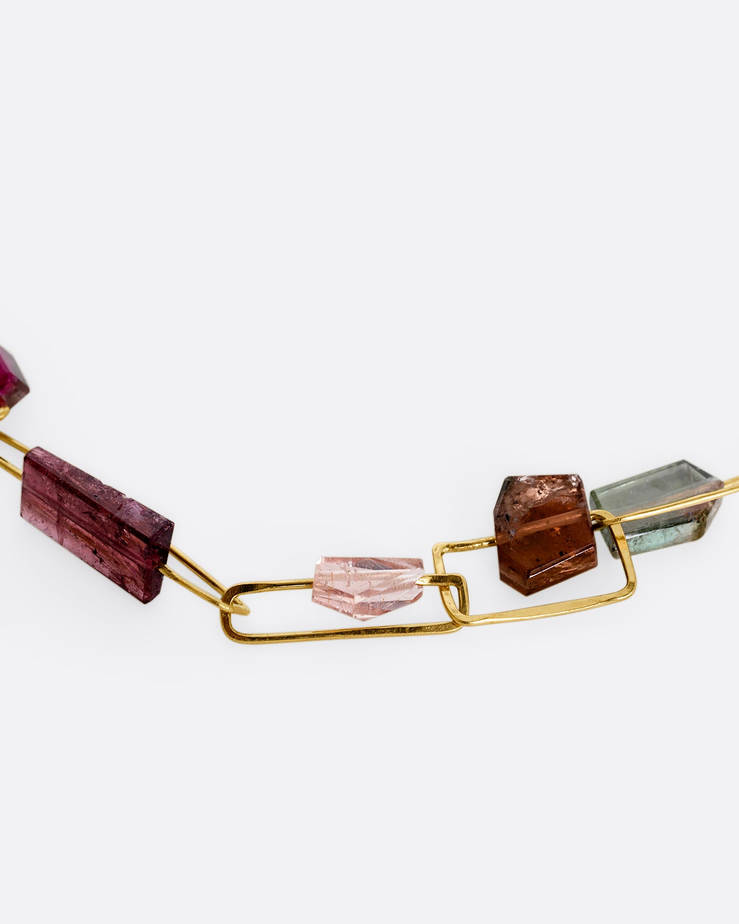 A yellow gold rectangular link necklace with multicolor and shape tourmalines. View of the stones close up.