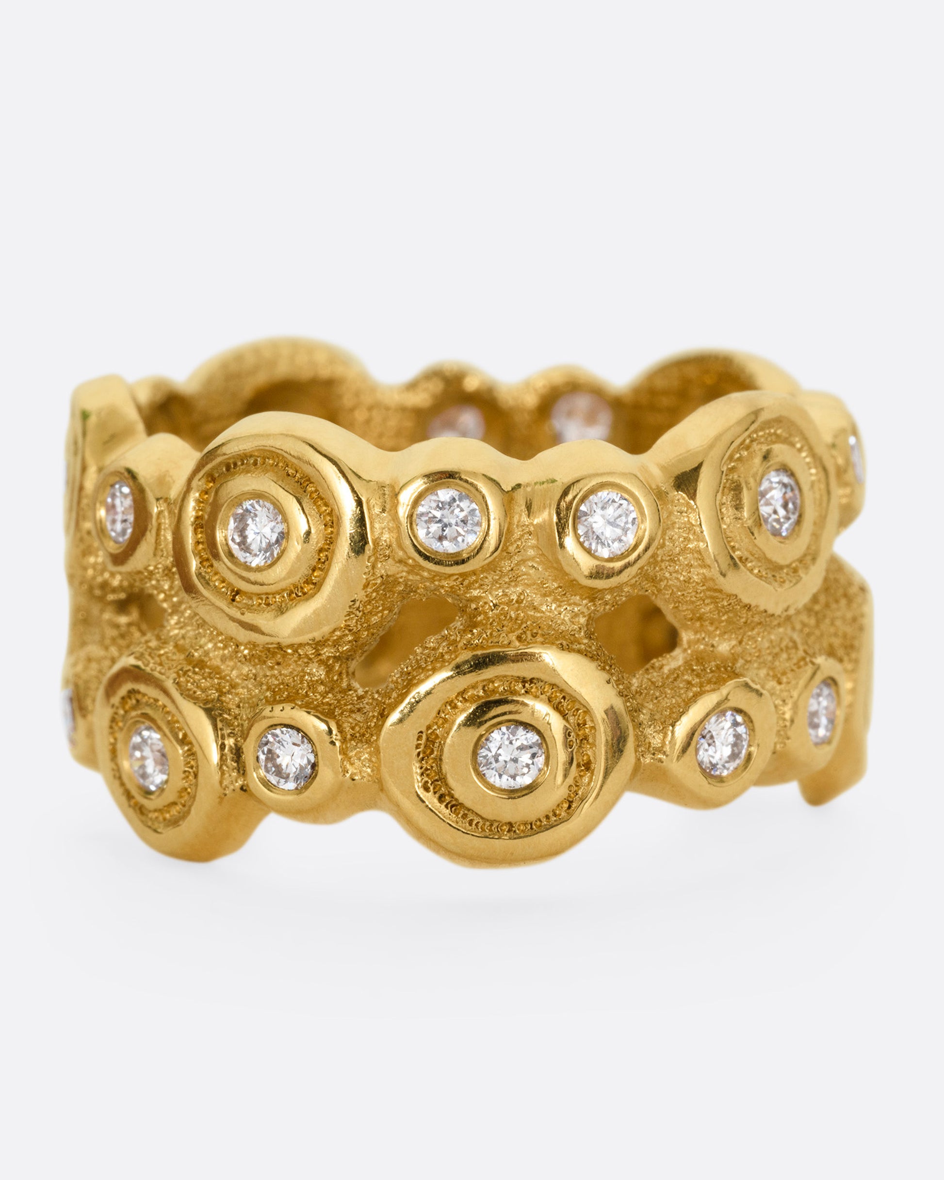 A wide yellow gold ring with brilliant cut diamonds nestled in bezel settings, shown from the front.