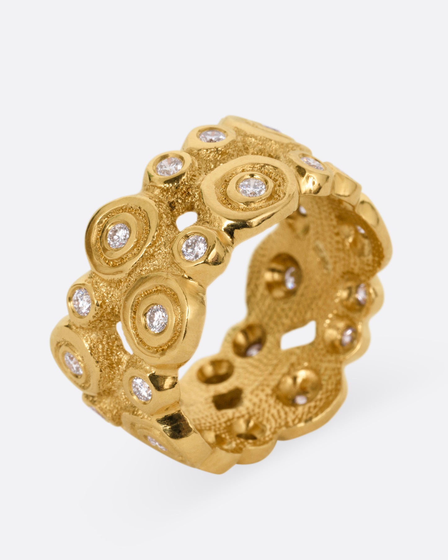 A wide yellow gold ring with brilliant cut diamonds nestled in bezel settings, shown standing up from the side.