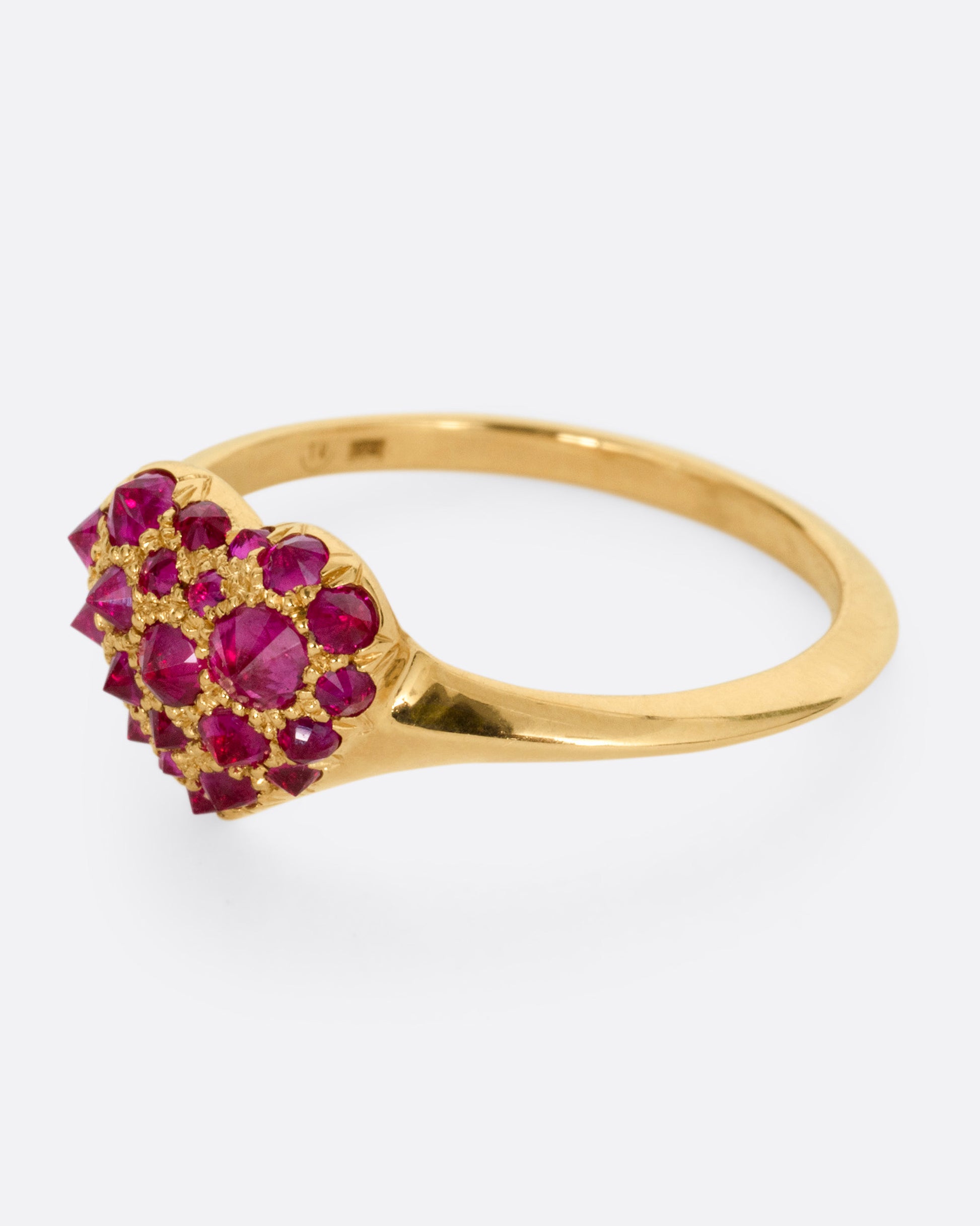 A yellow gold ring with a heart peppered with reverse set rubies of varying sizes, shown from the side.