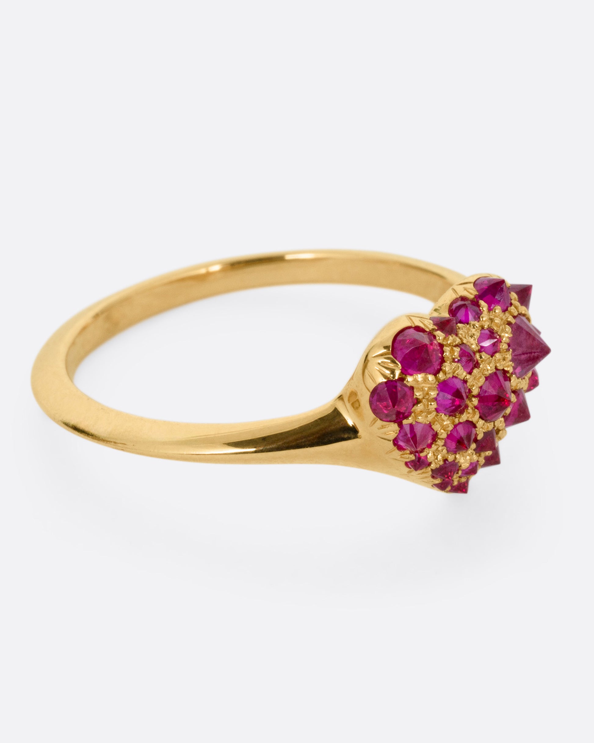 A yellow gold ring with a heart peppered with reverse set rubies of varying sizes, shown from the side.