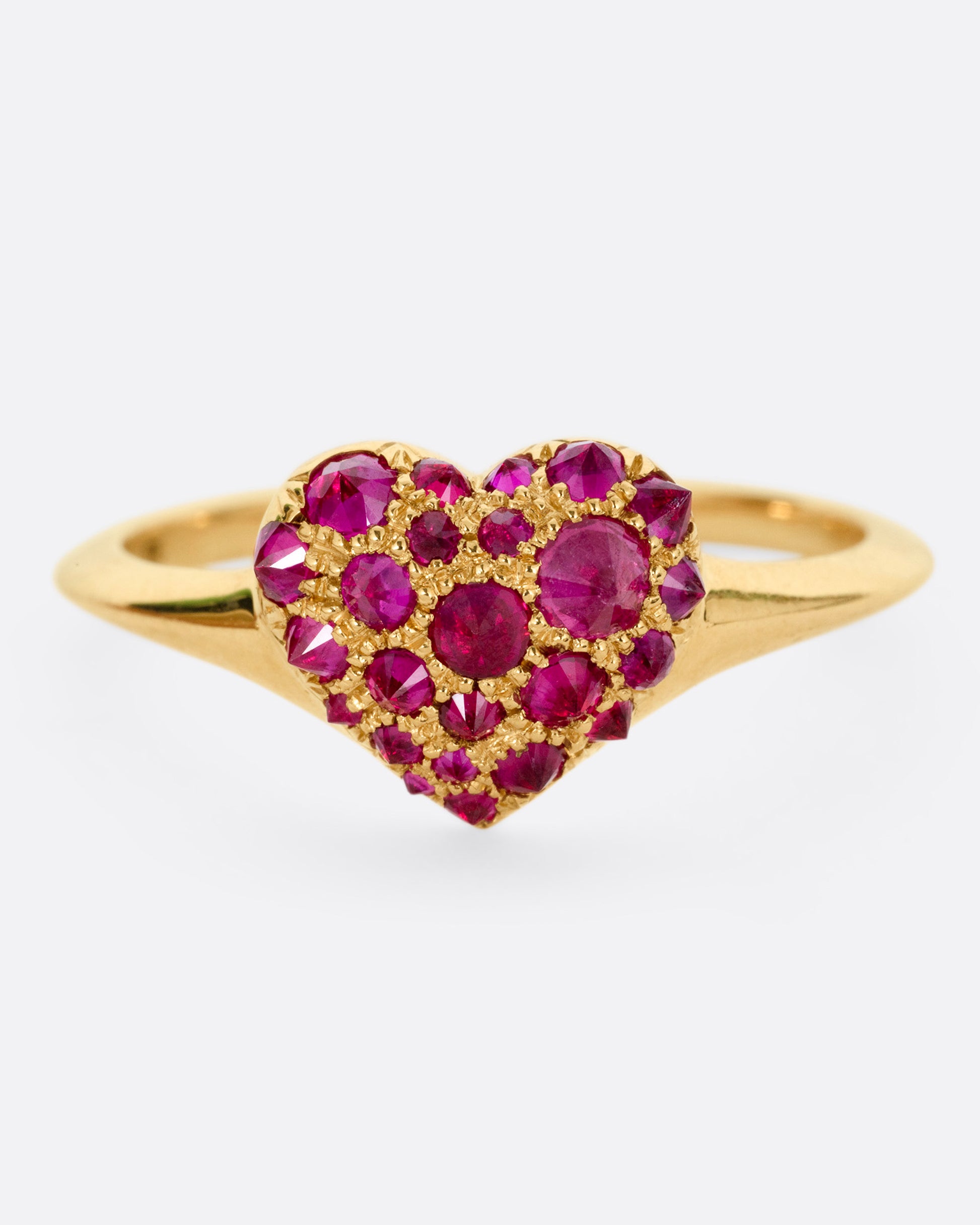 A yellow gold ring with a heart peppered with reverse set rubies of varying sizes, shown from the front.