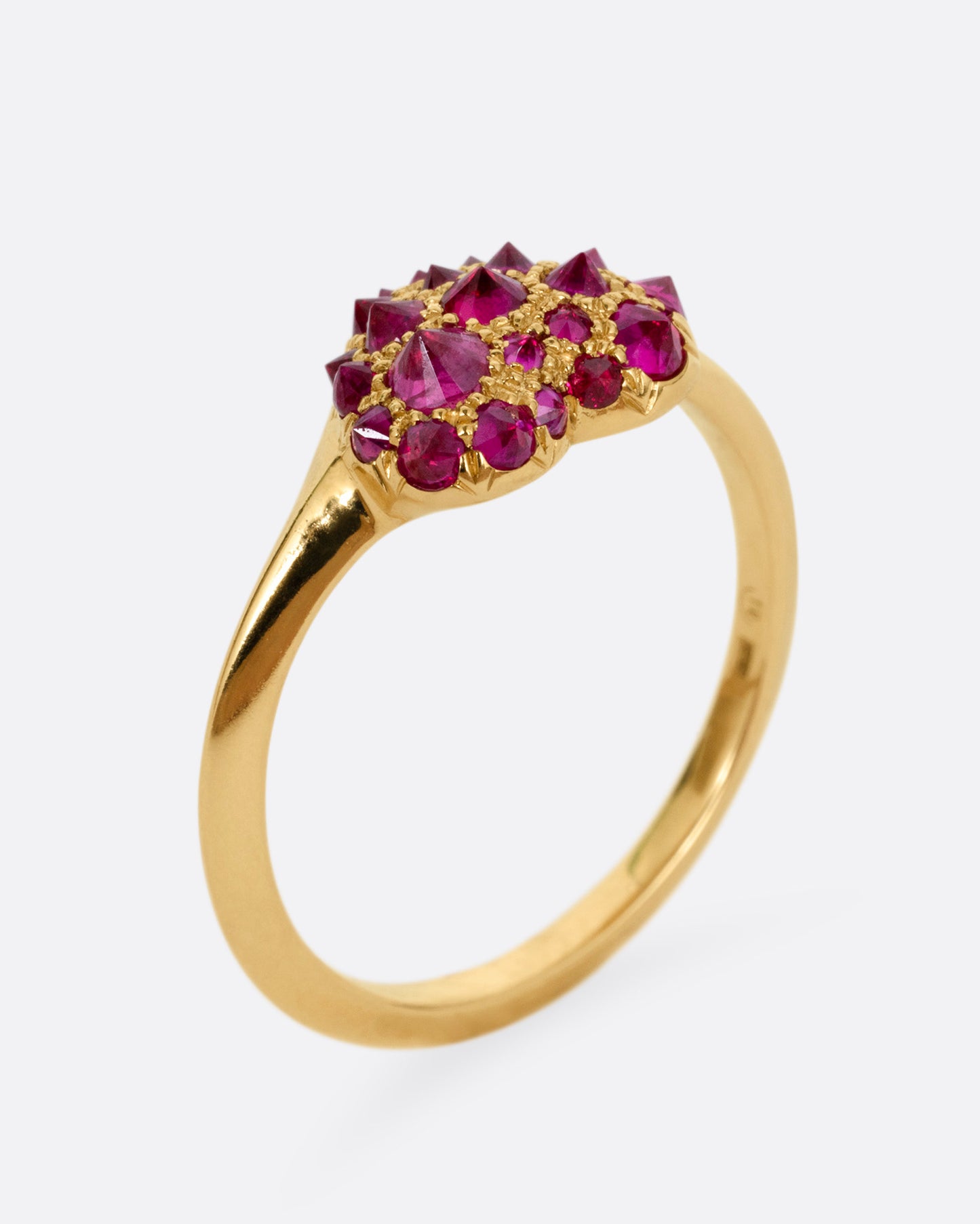 A yellow gold ring with a heart peppered with reverse set rubies of varying sizes, shown from the side standing up.