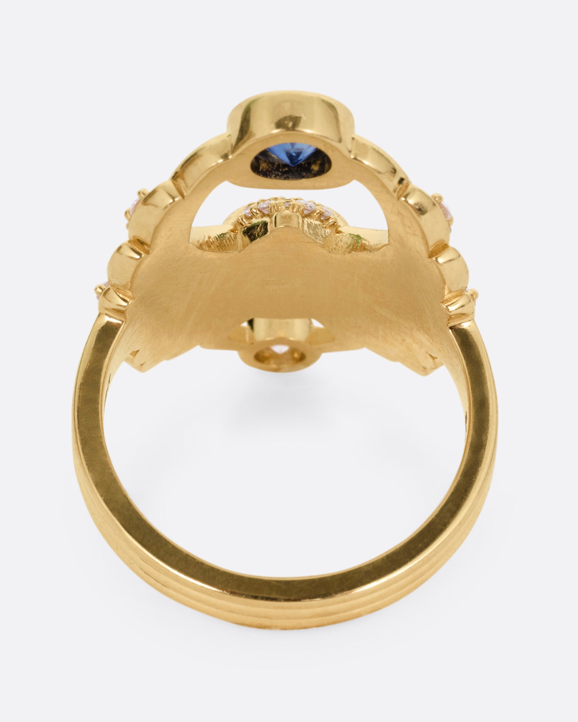 A yellow gold scarab ring with accents of white diamonds and a single blue sapphire between its fanned wings. Shown from the side.