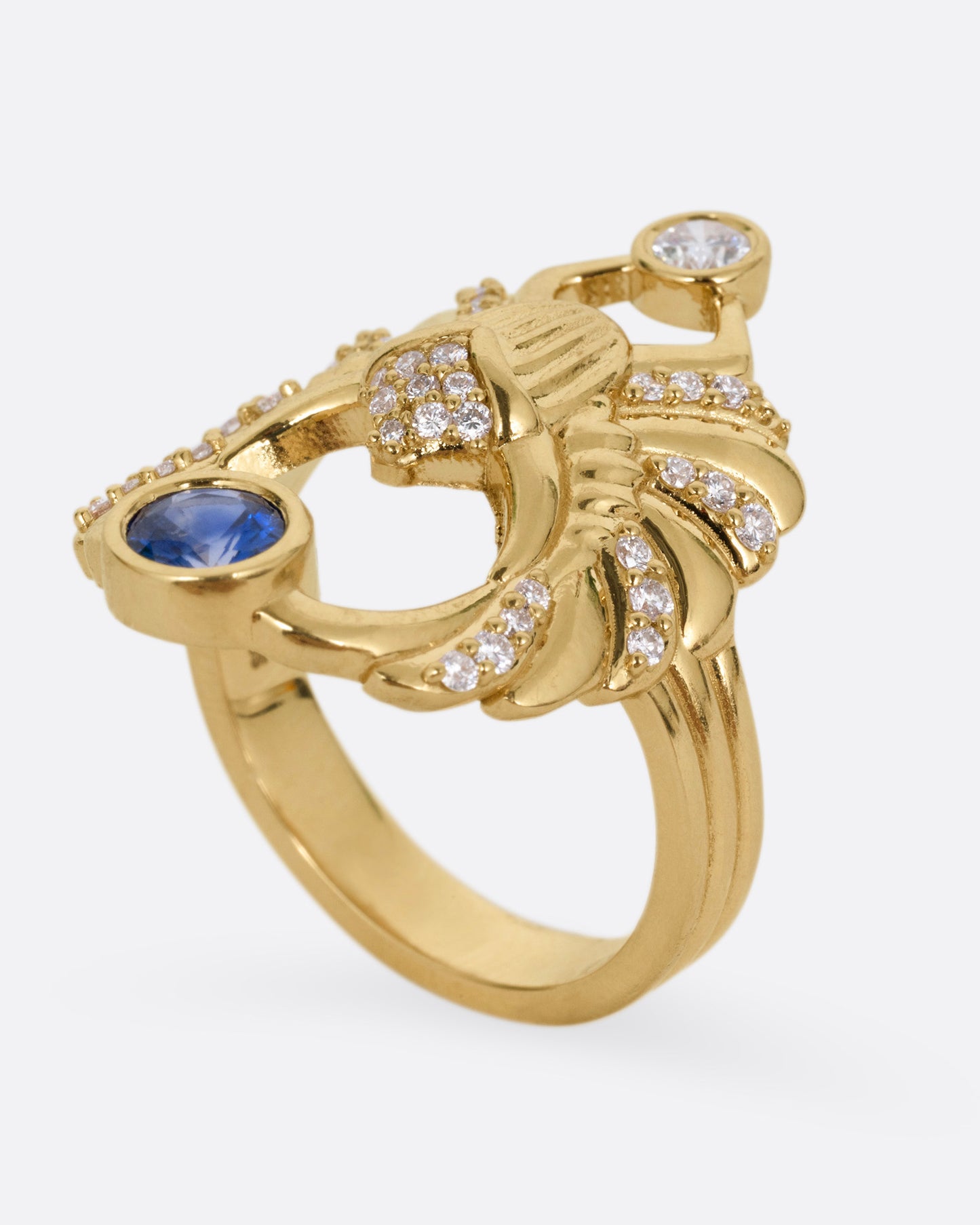 A yellow gold scarab ring with accents of white diamonds and a single blue sapphire between its fanned wings. Shown from the side standing up.