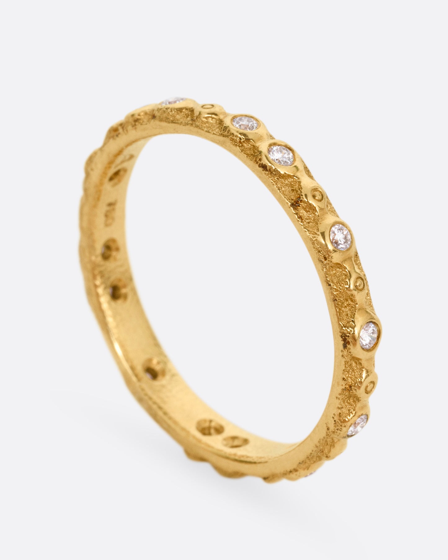 A textured yellow gold ring with white diamonds. Shown from the side standing up.