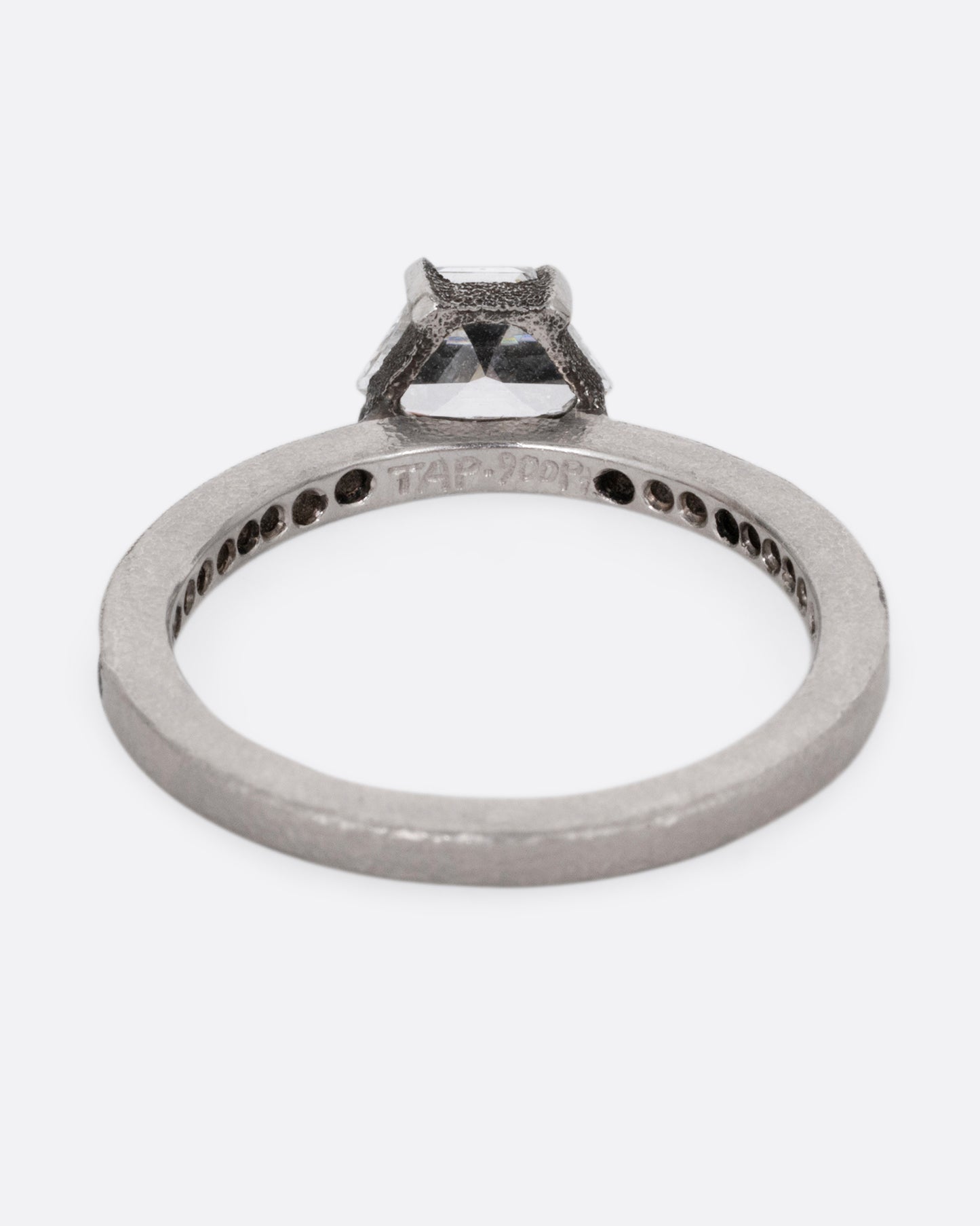 A platinum band with pave diamonds all the way around and a solitaire trapeze diamond. Shown from the back.