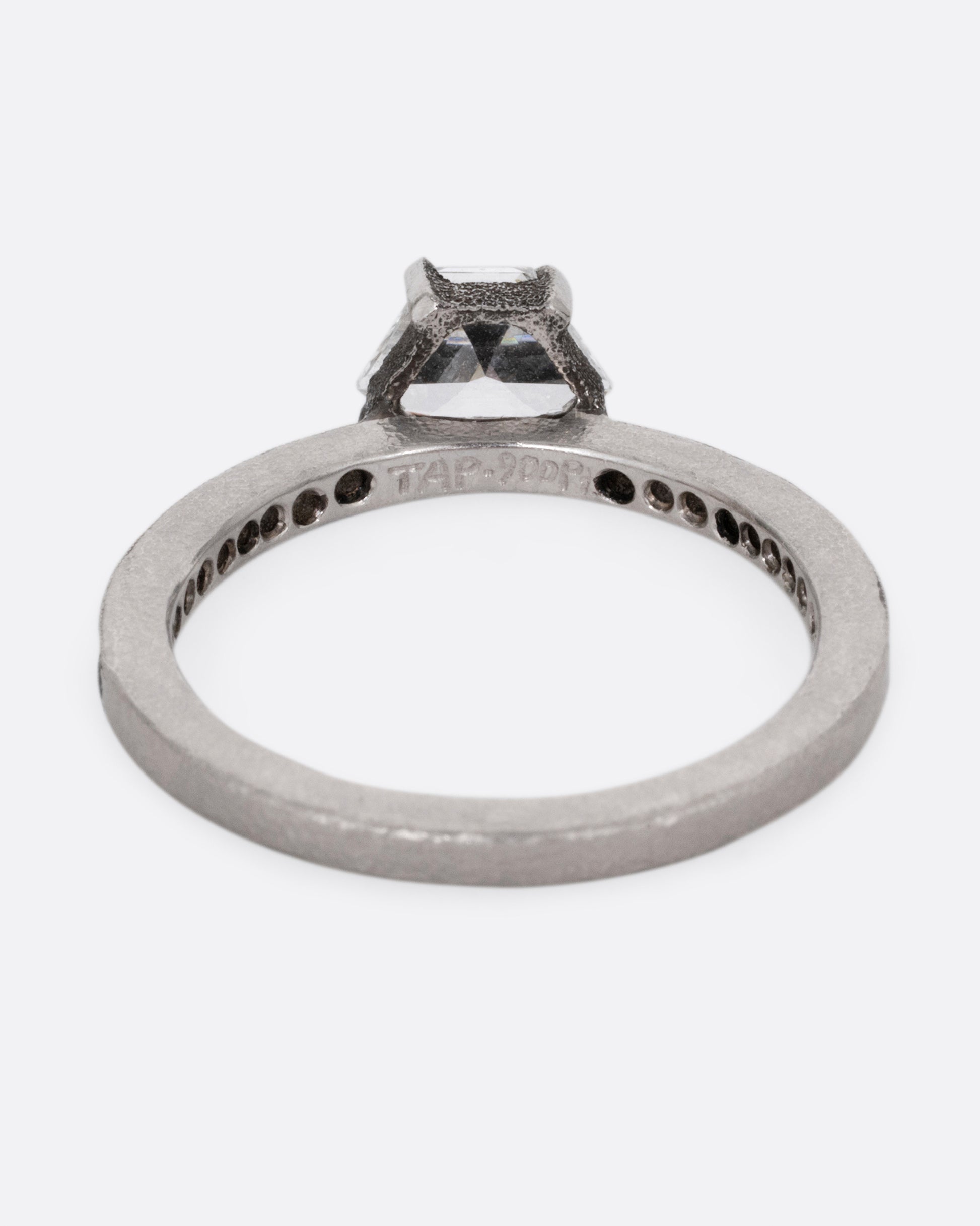 A platinum band with pave diamonds all the way around and a solitaire trapeze diamond. Shown from the back.