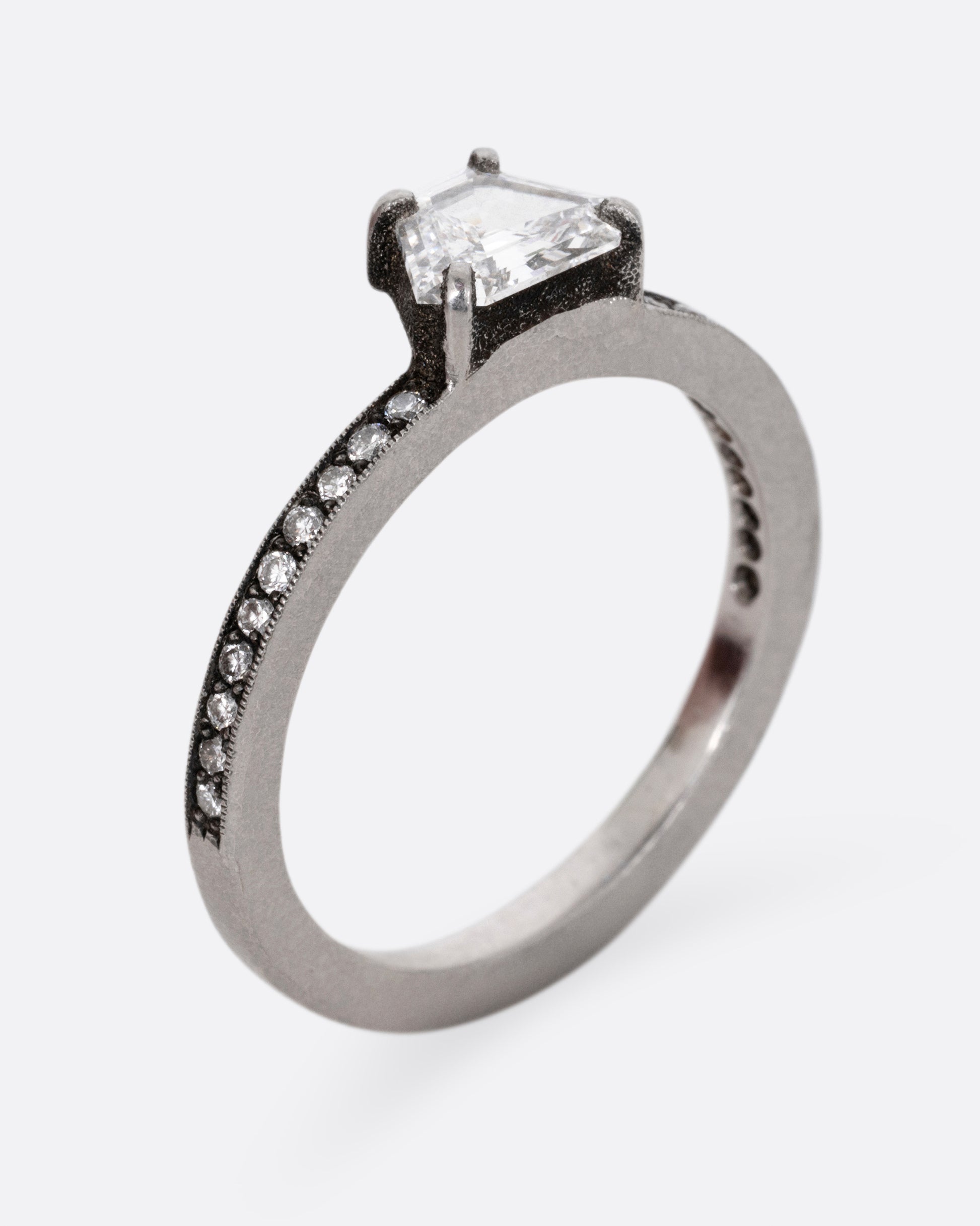A platinum band with pave diamonds all the way around and a solitaire trapeze diamond. Shown from the side, standing up.