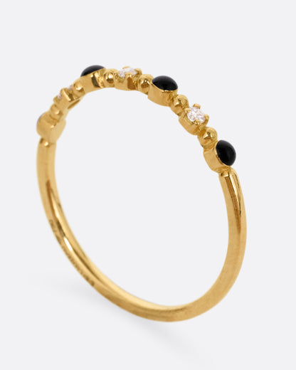 A yellow gold ring with three white diamonds and four black resin droplets, shown from the side standing up.