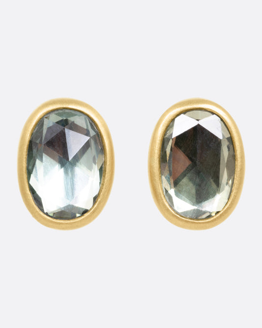 A pair of yellow gold stud earrings with pale green sapphires, shown from the front.