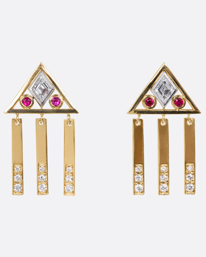 A yellow gold pair of stud back earrings with triangular tops set with lozenge cut diamonds flanked by rubies, and three free moving diamond studded bars on each base. Shown from the front.