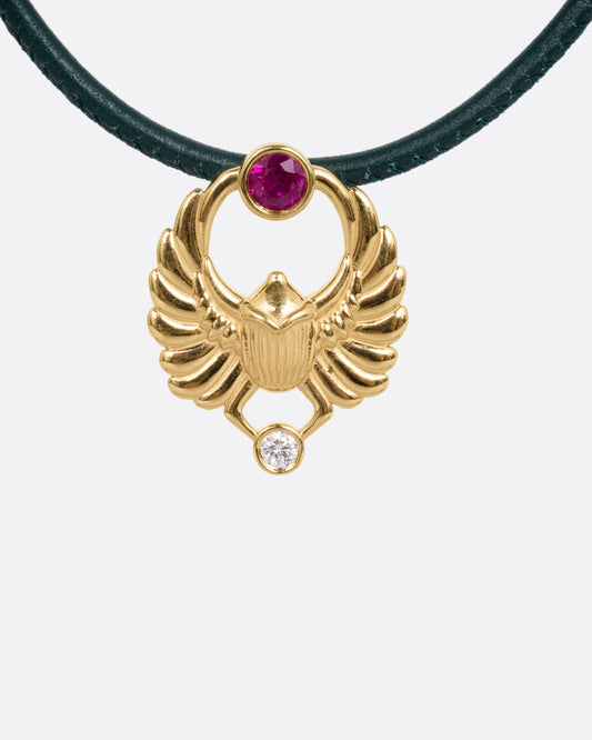 A yellow gold scarab pendant with a ruby and diamond, suspended from a green leather choker cord. Shown from the front.