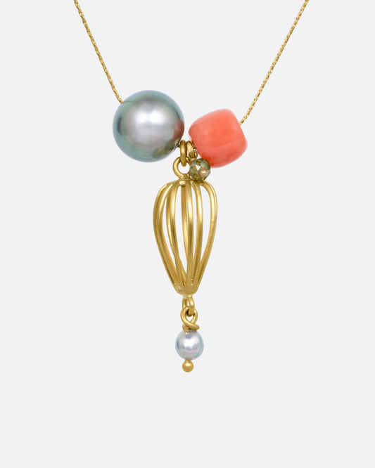 A yellow gold necklace with a gold pendant, Tahitian and Akoya pearls, a coral bead, and a green diamond bead, shown from the front.