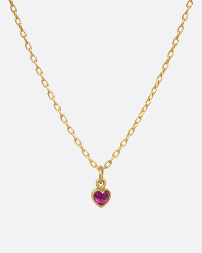 A yellow gold cable chain necklace with a tiny dimensional ruby heart, shown from the front.