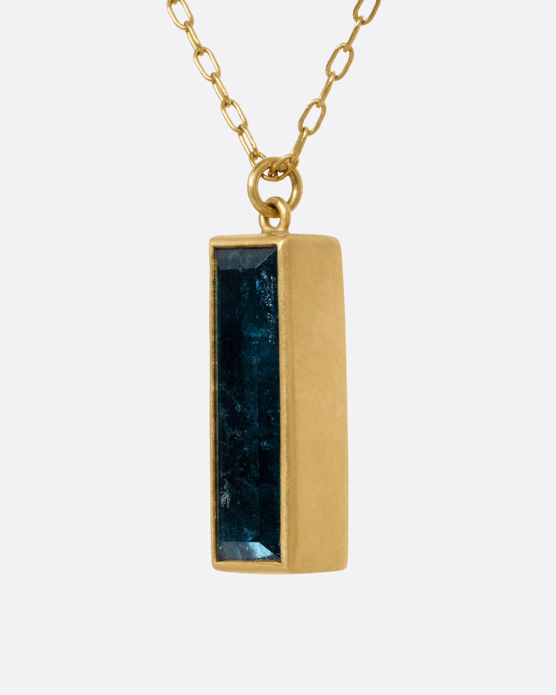 A yellow gold pendant necklace with a blue tourmaline slab, shown from the side.