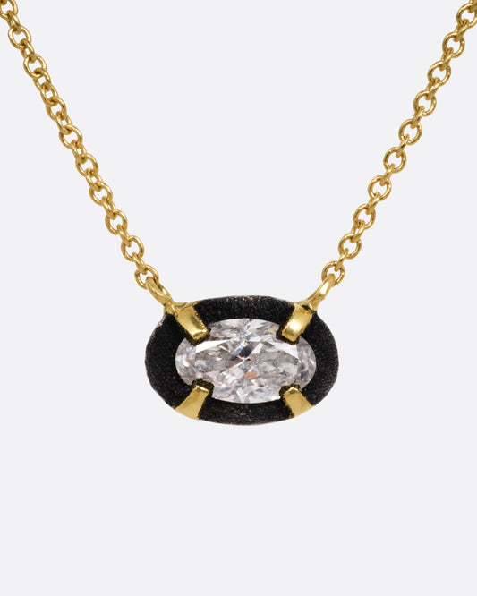 A yellow gold necklace with a pendant of darkened white gold surrounding a prong set diamond, shown from the front.