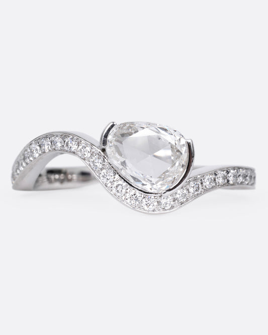 A diamond studded platinum ring with a wavy silhouette and a pear shaped rose cut diamond, shown from the front. 