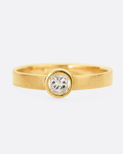 front view of a round yellow gold hole has a diamond set floating into the middle of it. there is a medium wide band that the setting is attached to and the gold is matte.