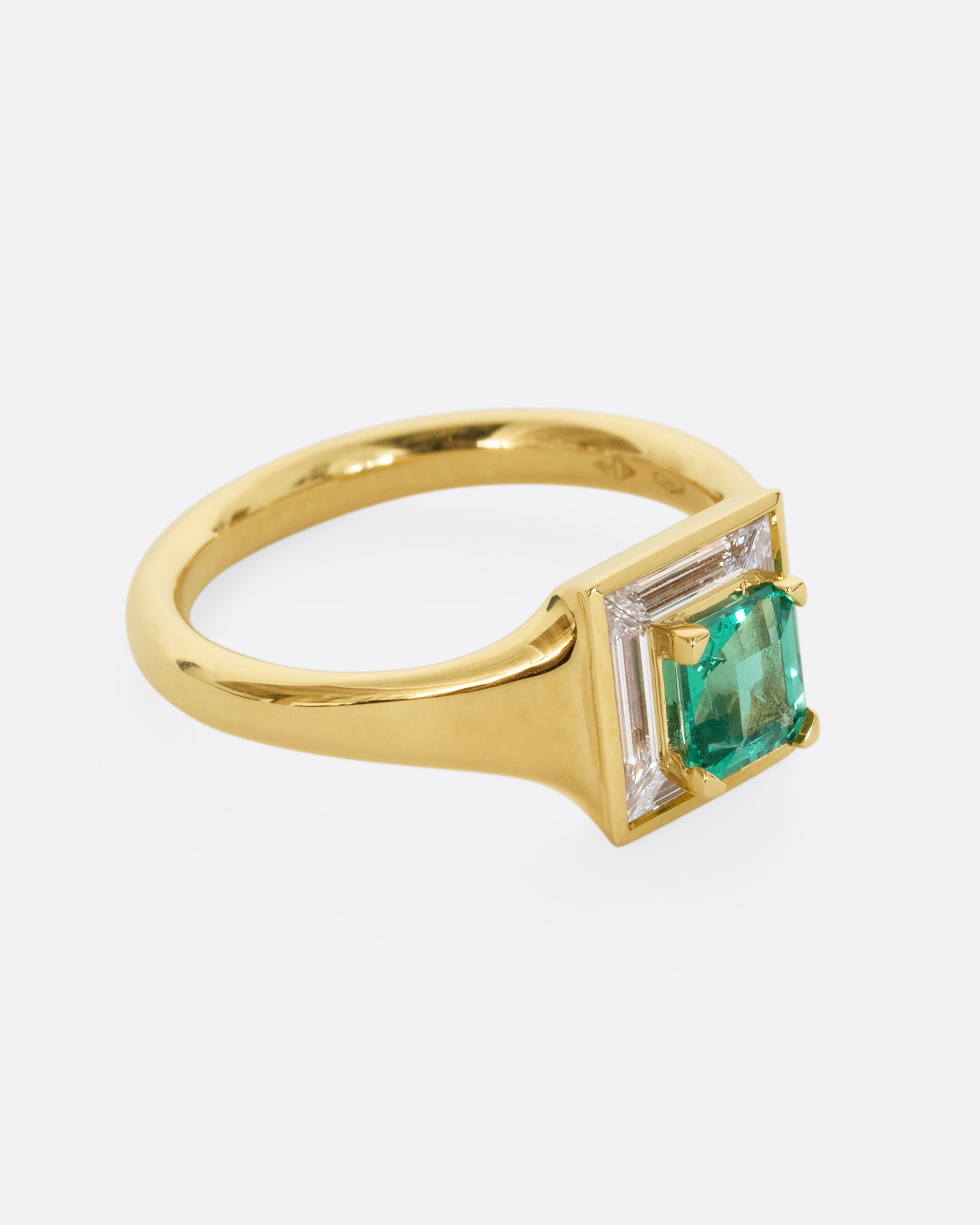 A yellow gold ring with a square emerald at the center surrounded by white baguette diamonds. Shown from the side.