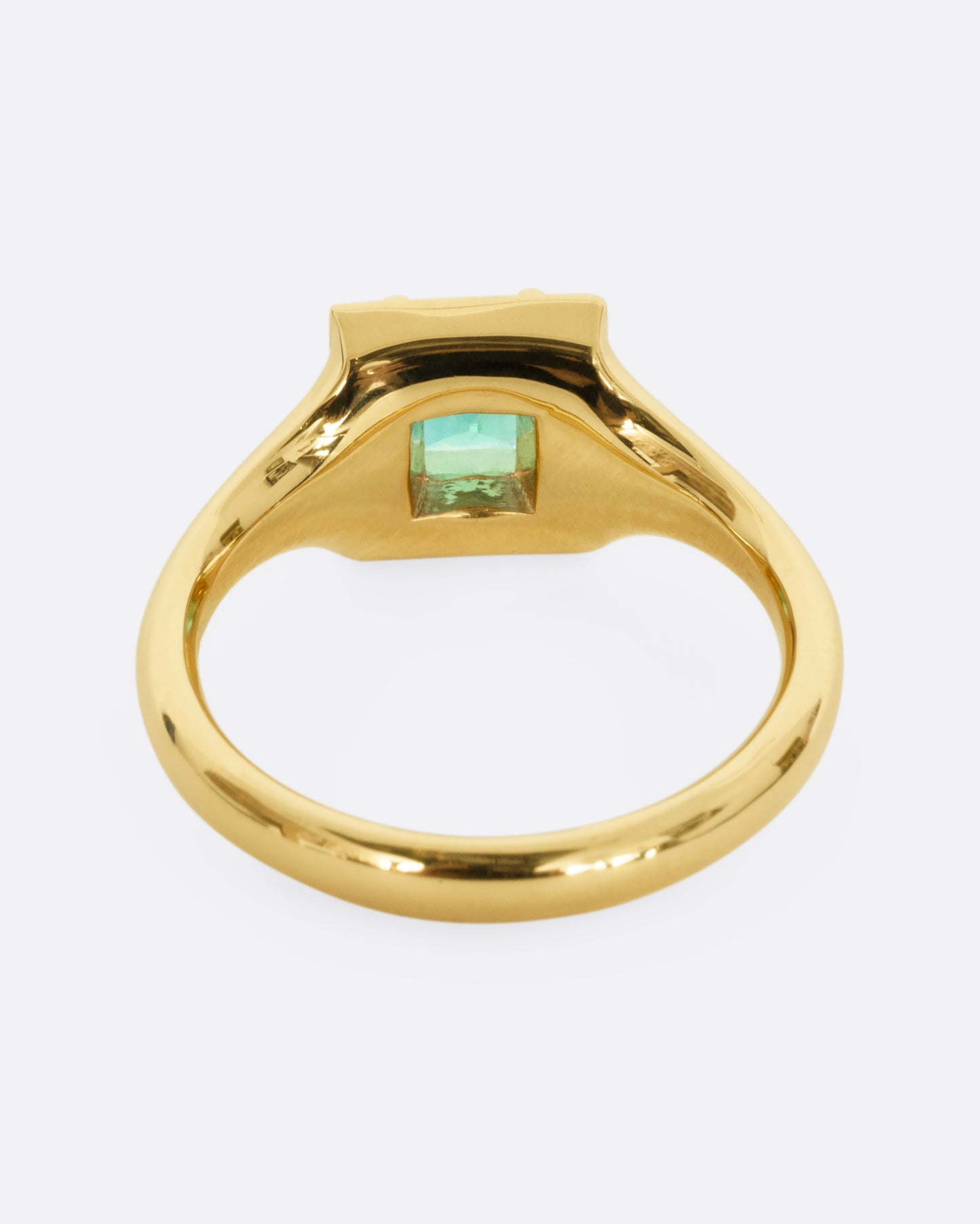 A yellow gold ring with a square emerald at the center surrounded by white baguette diamonds. Shown from the back.