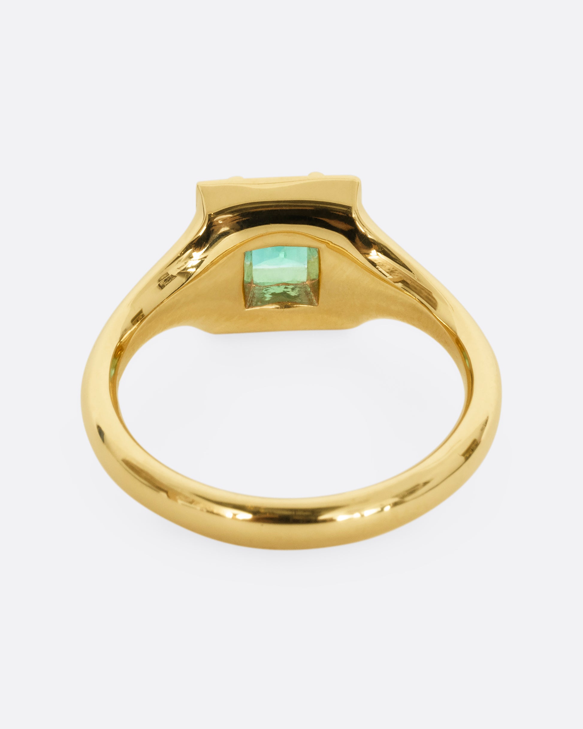 A yellow gold ring with a square emerald at the center surrounded by white baguette diamonds. Shown from the back.