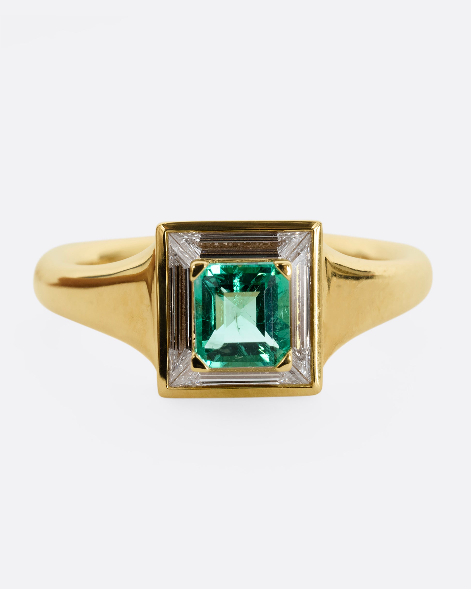 A yellow gold ring with a square emerald at the center surrounded by white baguette diamonds. Shown from the front.