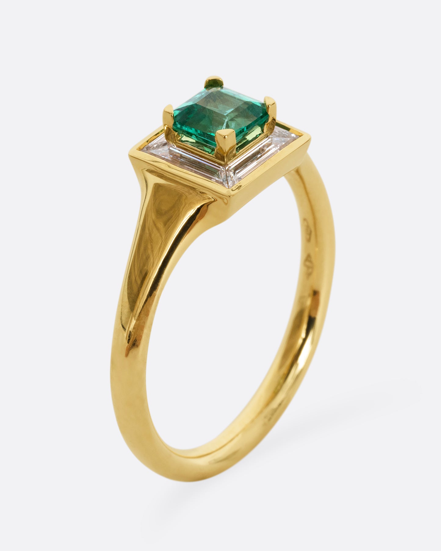 A yellow gold ring with a square emerald at the center surrounded by white baguette diamonds. Shown from the side, standing up.