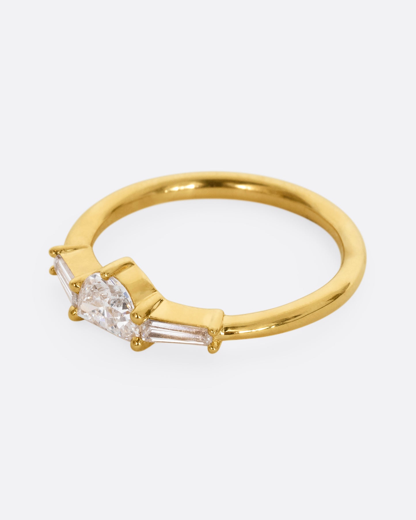 A yellow gold ring with a half moon shaped diamond and two baguette diamonds. Shown from the side.