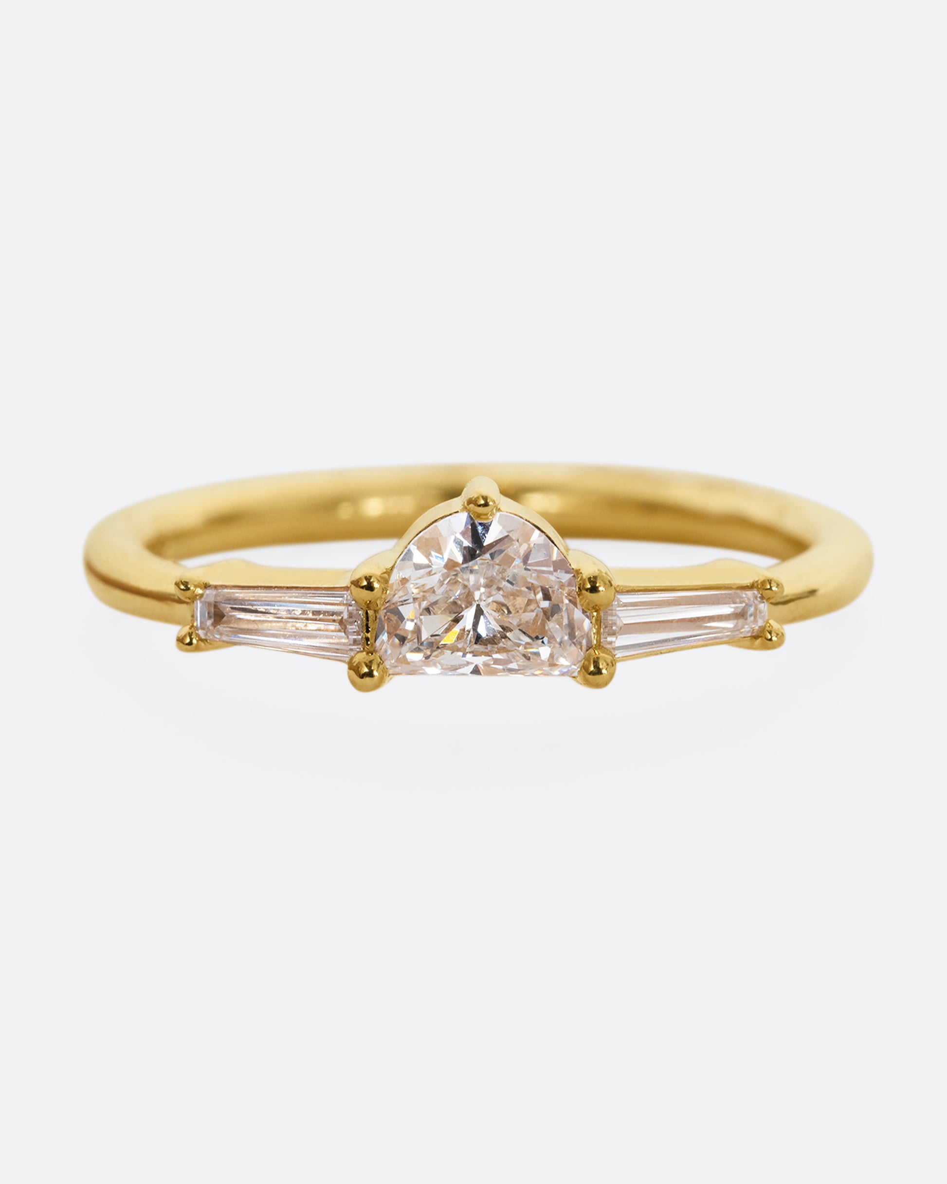 A yellow gold ring with a half moon shaped diamond and two baguette diamonds. Shown from the front.