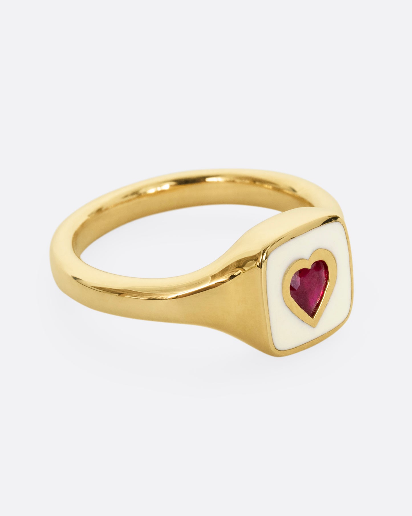 A yellow gold signet ring with cream enamel and a heart shaped ruby. Shown from the side.